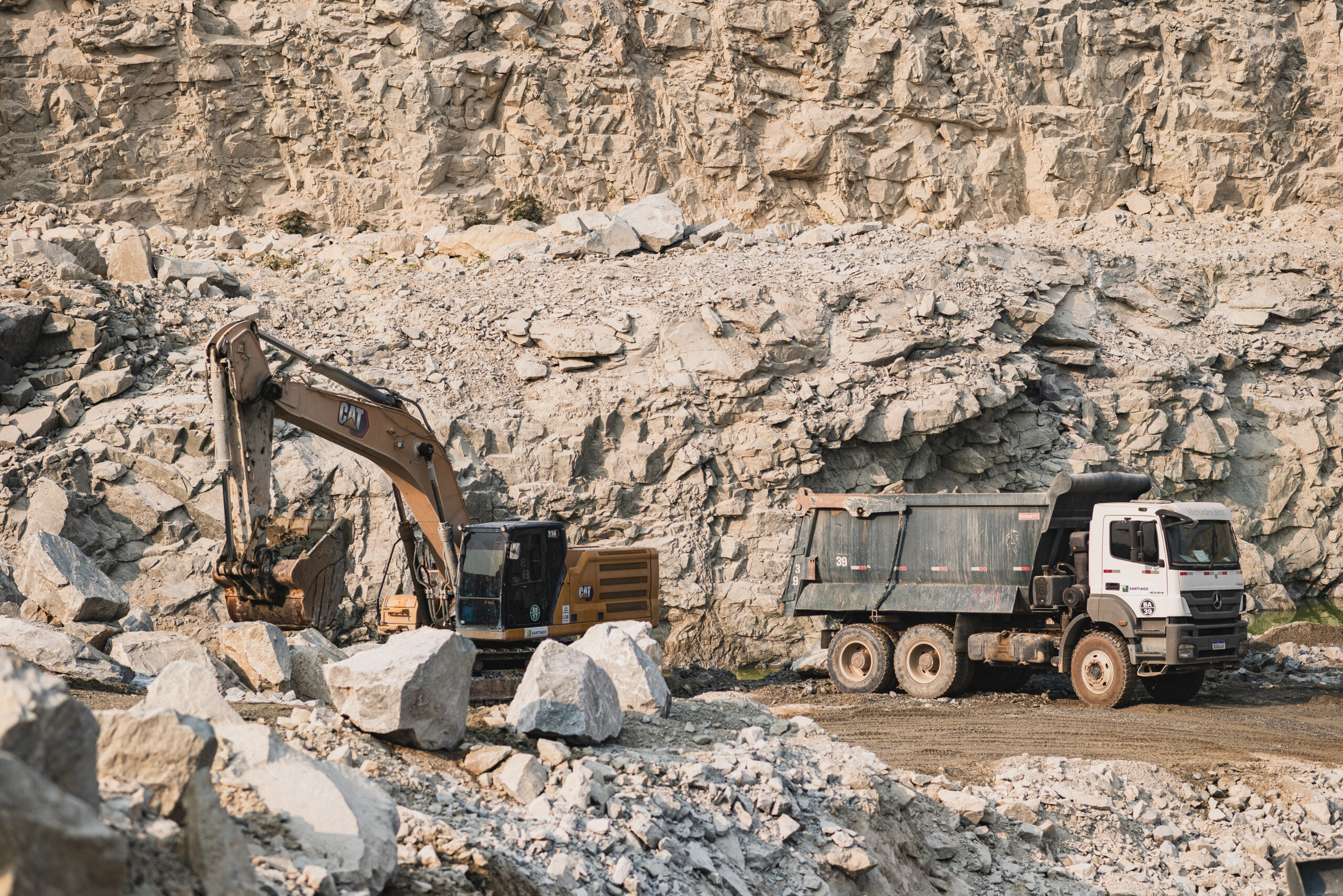 Operação eficiente em mina de céu aberto da Mineração Santiago, com escavadeira e caminhão trabalhando para garantir o fornecimento sustentável de matérias-primas.