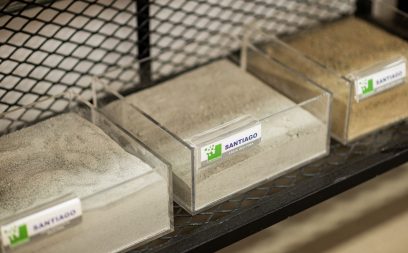 Amostras de Areia Industrial Amostras de Areia Industrial Fina Santiago e Areia Santiago em caixas de acrílico transparente em uma prateleira, mostrando diferentes texturas e granulometrias para construção.